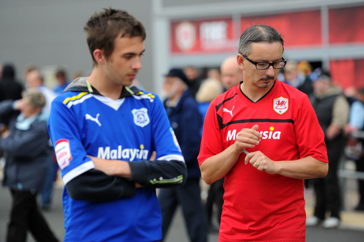 Two Cardiff City fans, one wearing the club's traditional blue home shirt and one wearing the club's new red home shirt following a controversial change by the club's owners, August 2012