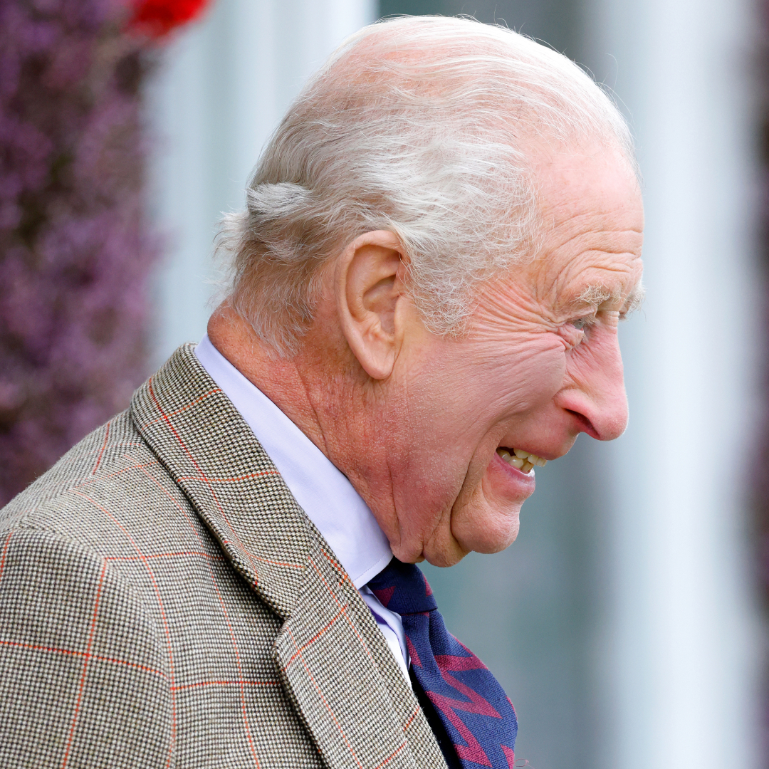 King Charles smiling in a suit and blue tie