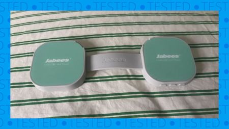 The image shows the flat green and white dumbbell-shaped Jabees PEACE Duo Pillow Speaker on a green and white striped comforter
