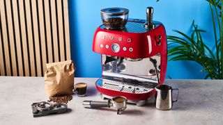 a red smeg espresso machine with burr grinder is photographed against a blue background