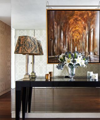 Mirror wall behind black lacquer sideboard with lamps flanking brown hue perspective painting and dark wood floor