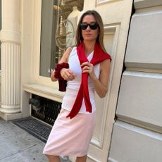 a woman wearing a white tank top, pink skirt, red sweater wrapped around her shoulder and black sunglasses
