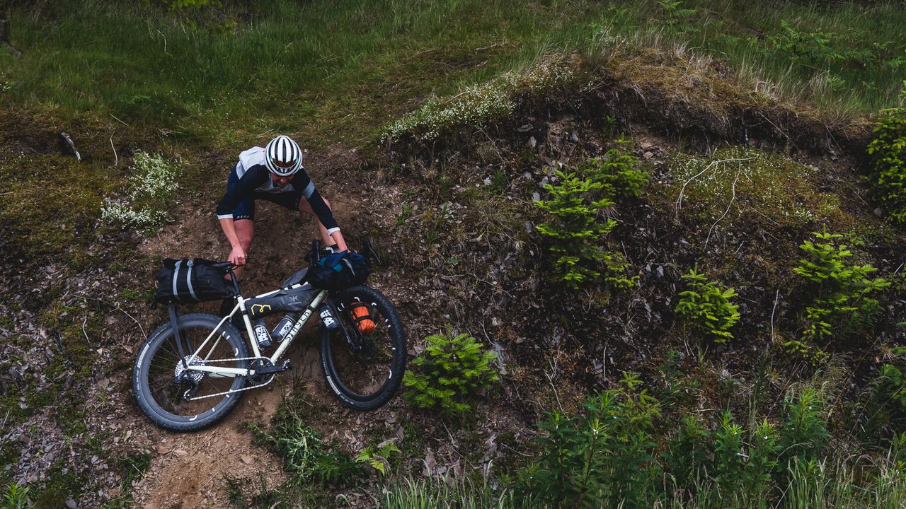 A cyclists lowers their bike down a steep embankment