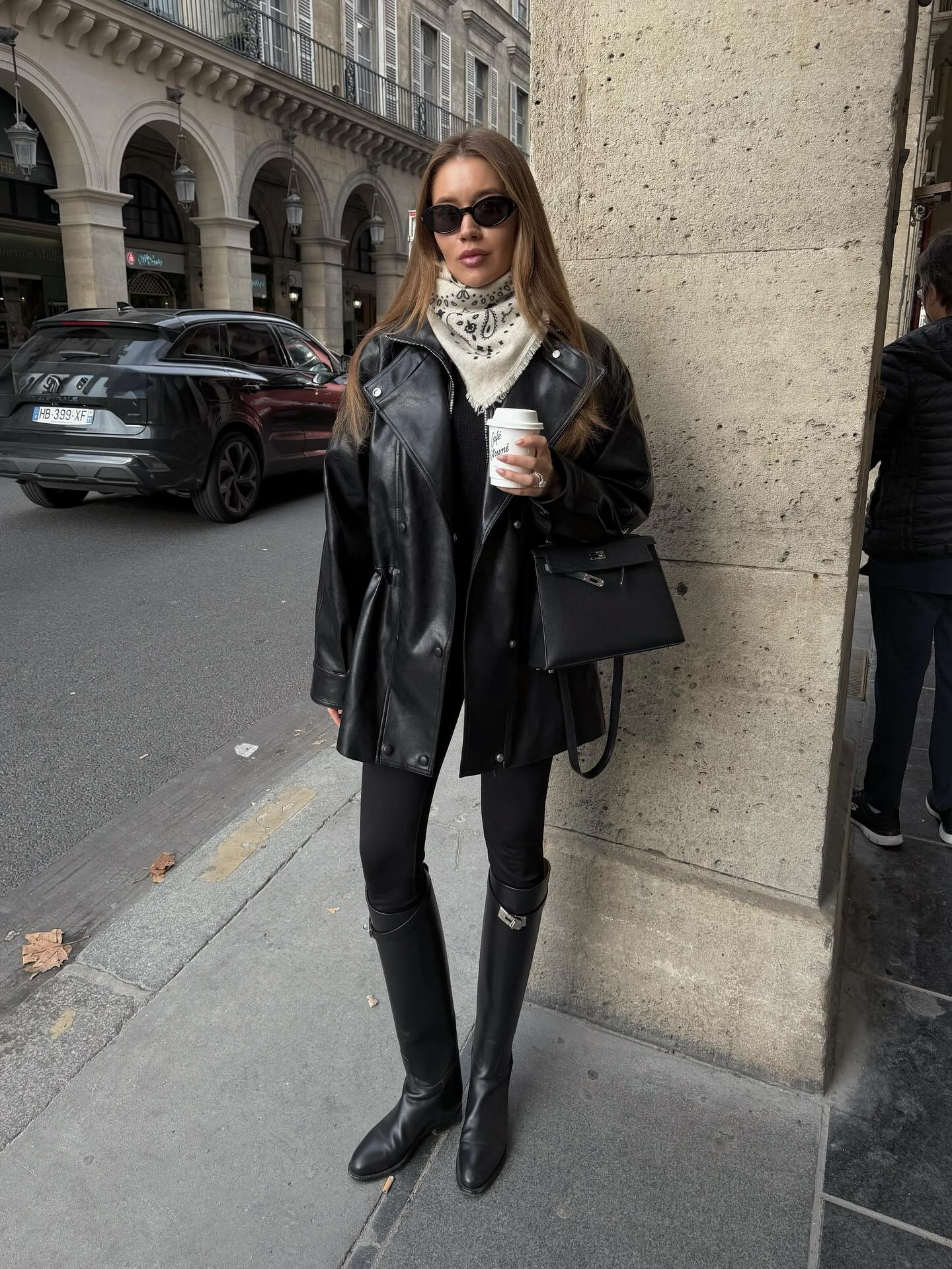 Influencer wearing white Kujten bandana neck scarf with black leather jacket, black leggings, black boots, and black handbag standing on the streets of Paris, France.