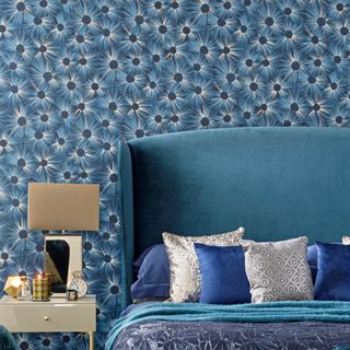 A bedroom with blue patterned wallpaper and a bed with a teal velvet headboard