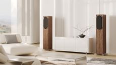 A pair of Loewe Inicio speakers in wood finish in a brightly lit room surrounded by very light coloured furniture