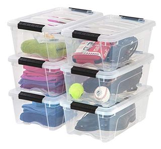 six Clear plastic storage bins with lids and black clip handles. Stacked in threes. full of sports equiptment