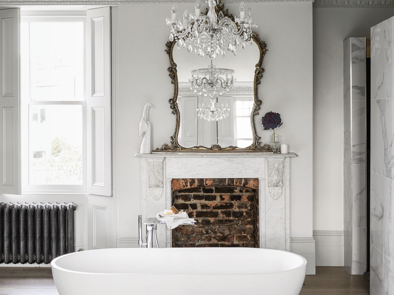 An all-white bathroom with a white bathtub, and a crystal chandelier