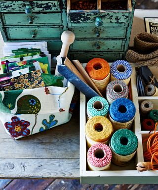 An aerial view of colorful twine and fabrics on a wooden table with mint green painted storage drawers.