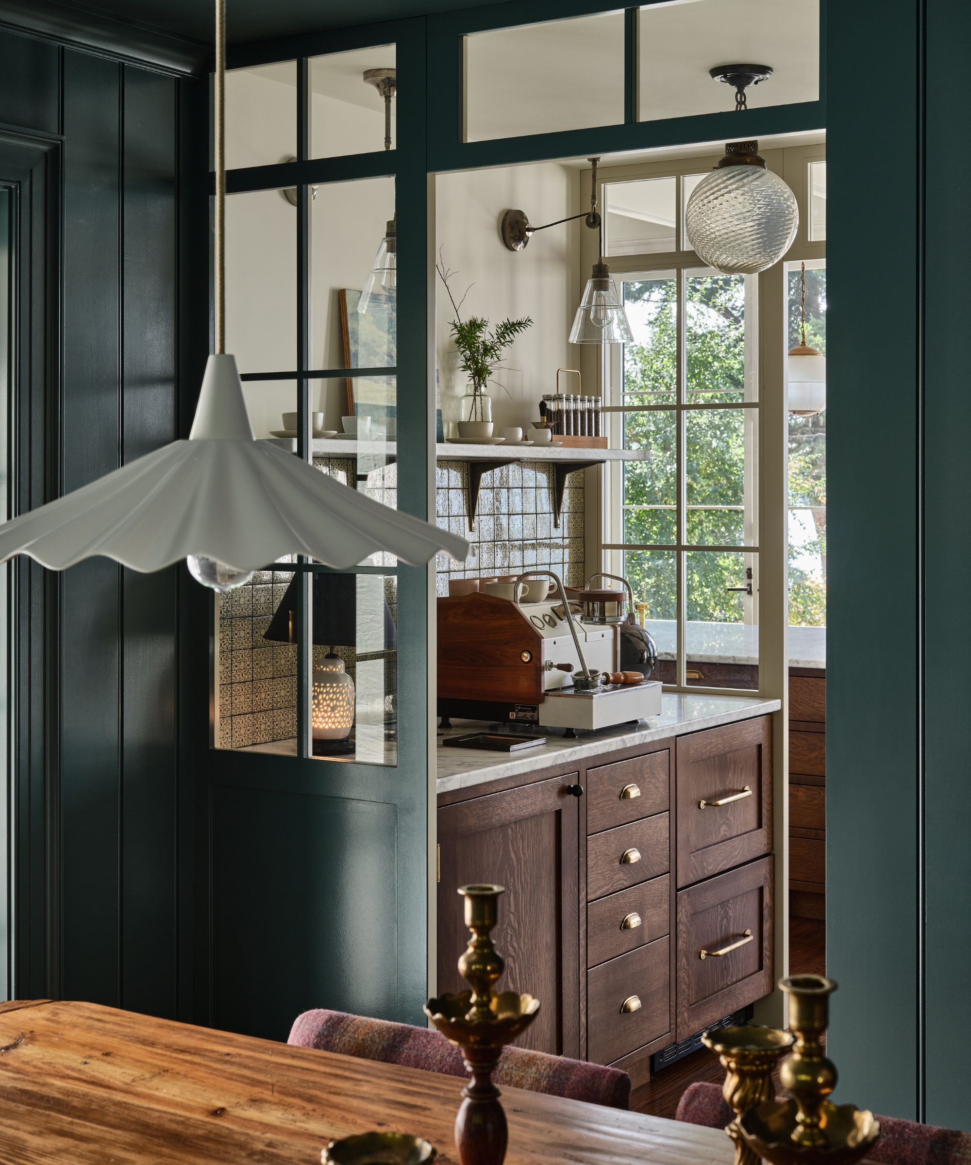 A view looking from a dark teal-paneled dining room into a kitchen, highlighting a wooden coffee station with an espresso machine