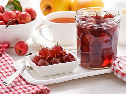 A bowl of fresh crabapples, a dish of preserved crabapples, and an open jar of crabapples in syrup