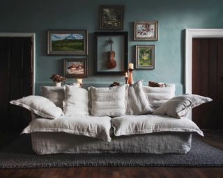 A rumpled linen sofa with large cushions in front of a dark teal wall in a period property