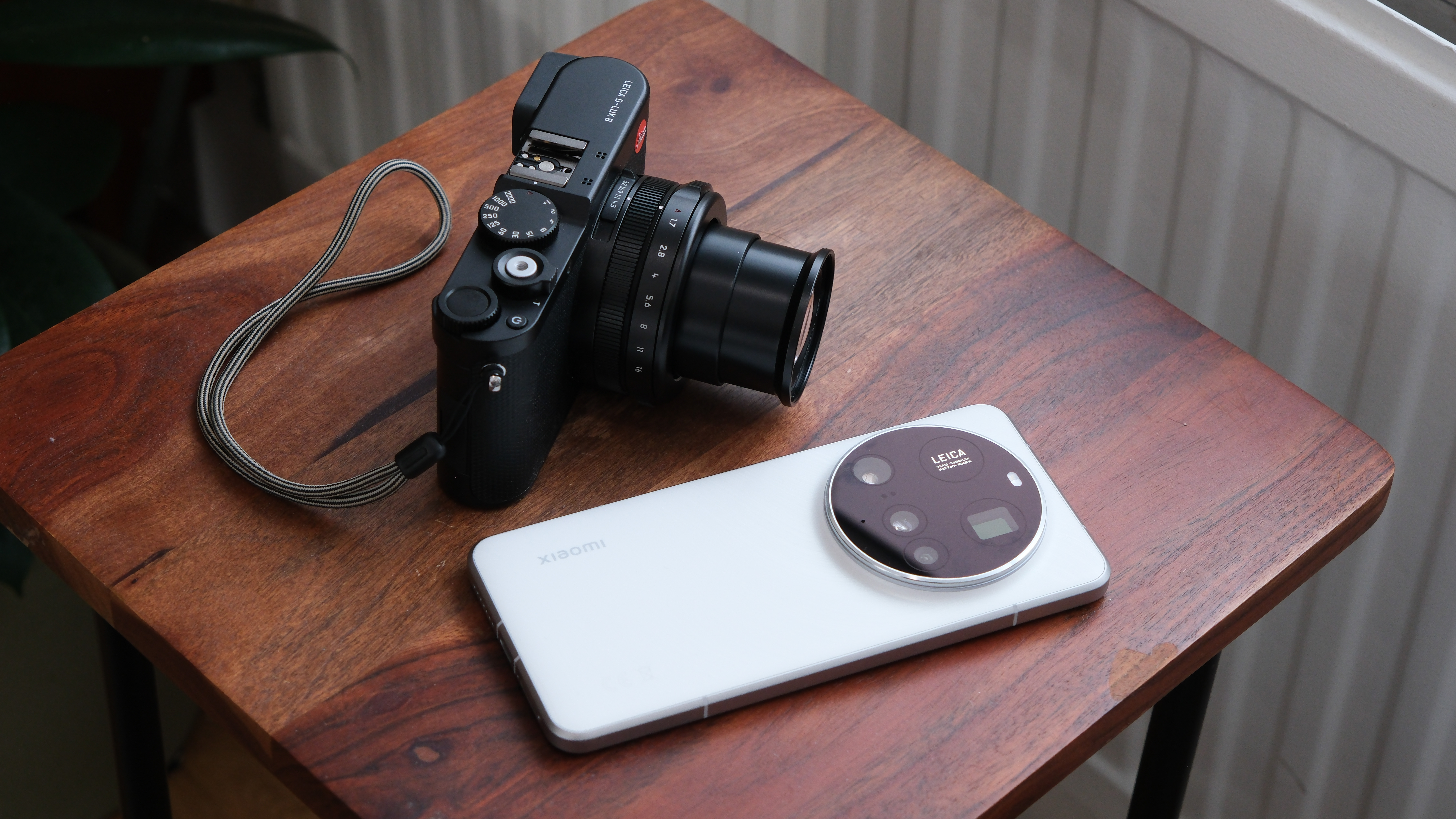 Leica D-Lux 8 camera next to a Xiaomi 15 Ultra phone on a wooden table