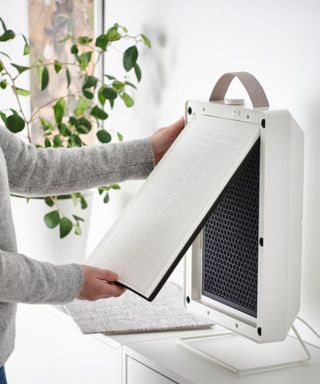 A man assembling an IKEA air purifier against a white wall.