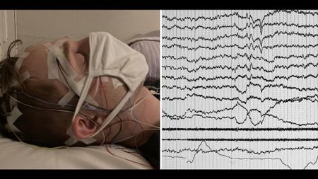 A participant sleeping in the lab as electrical signals from his brain and eyes are displayed on a computer monitor. 