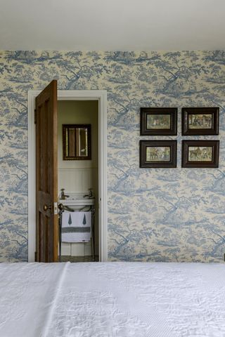 bedroom with blue toile wallpaper with wooden door into en suite bathroom