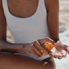 best waterproof sunscreens - Close up of woman wearing white swimming costume dispensing sun cream into her hand