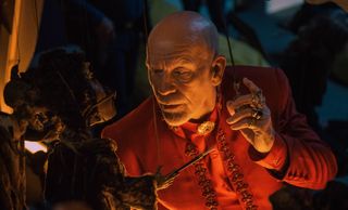 john malkovich in a red suit looking at a puppet of a rat in a still from opus