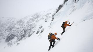 Two people ice climbing up a snowy mountain