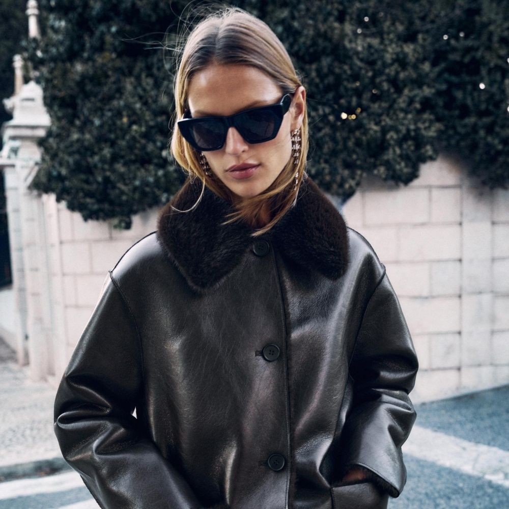 Woman wears cream coat with high collar, black trousers