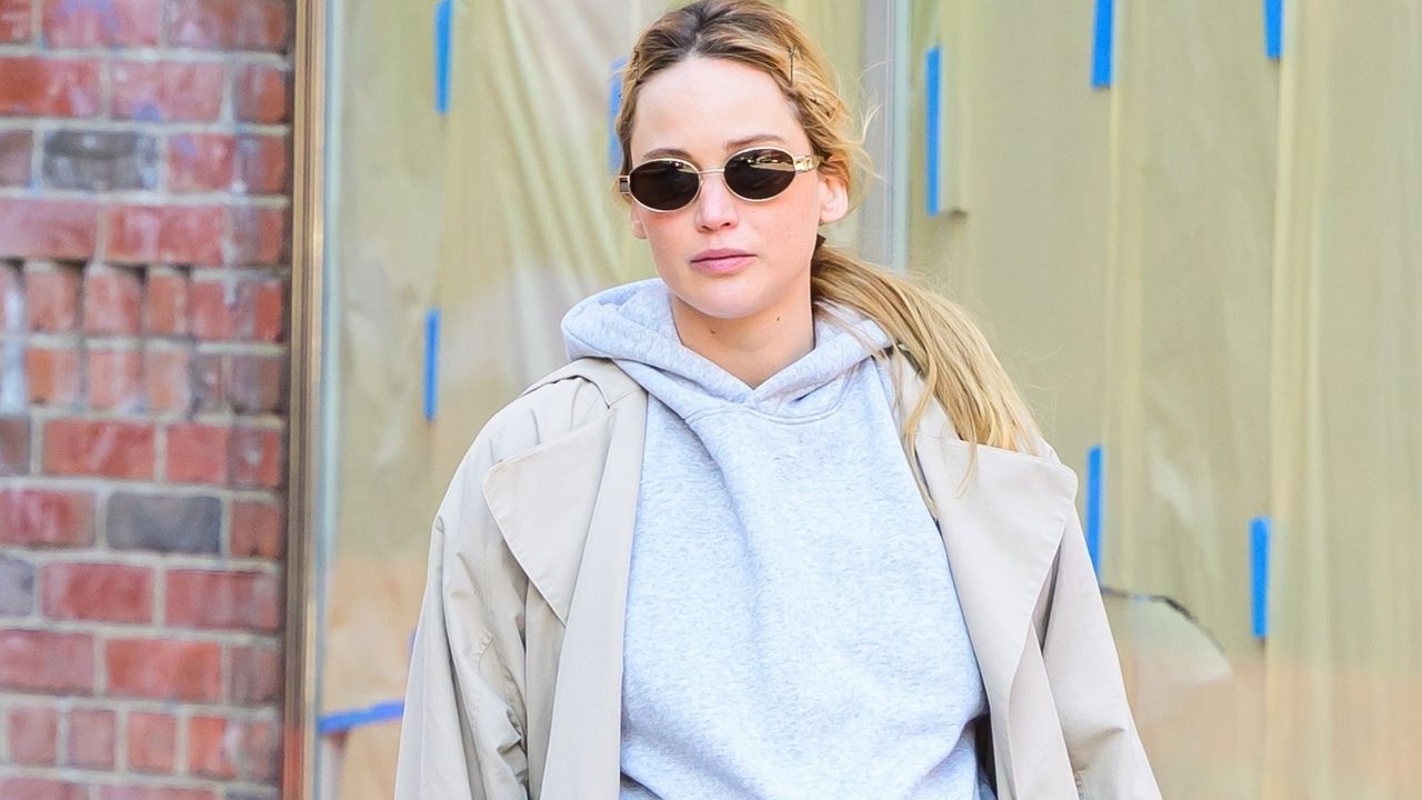 Jennifer Lawrence wears a trench coat with a hoodie and leopard print bag while walking around New York City