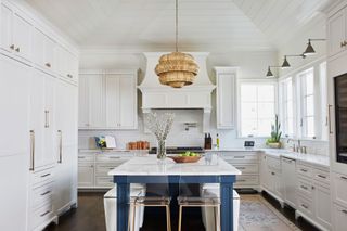white kitchen with vaulted ceiling island with blue legs and bar stools white cabinets and rattan pendant lamp