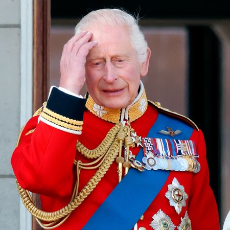 King Charles looks sad and holds his head while wearing a red military uniform