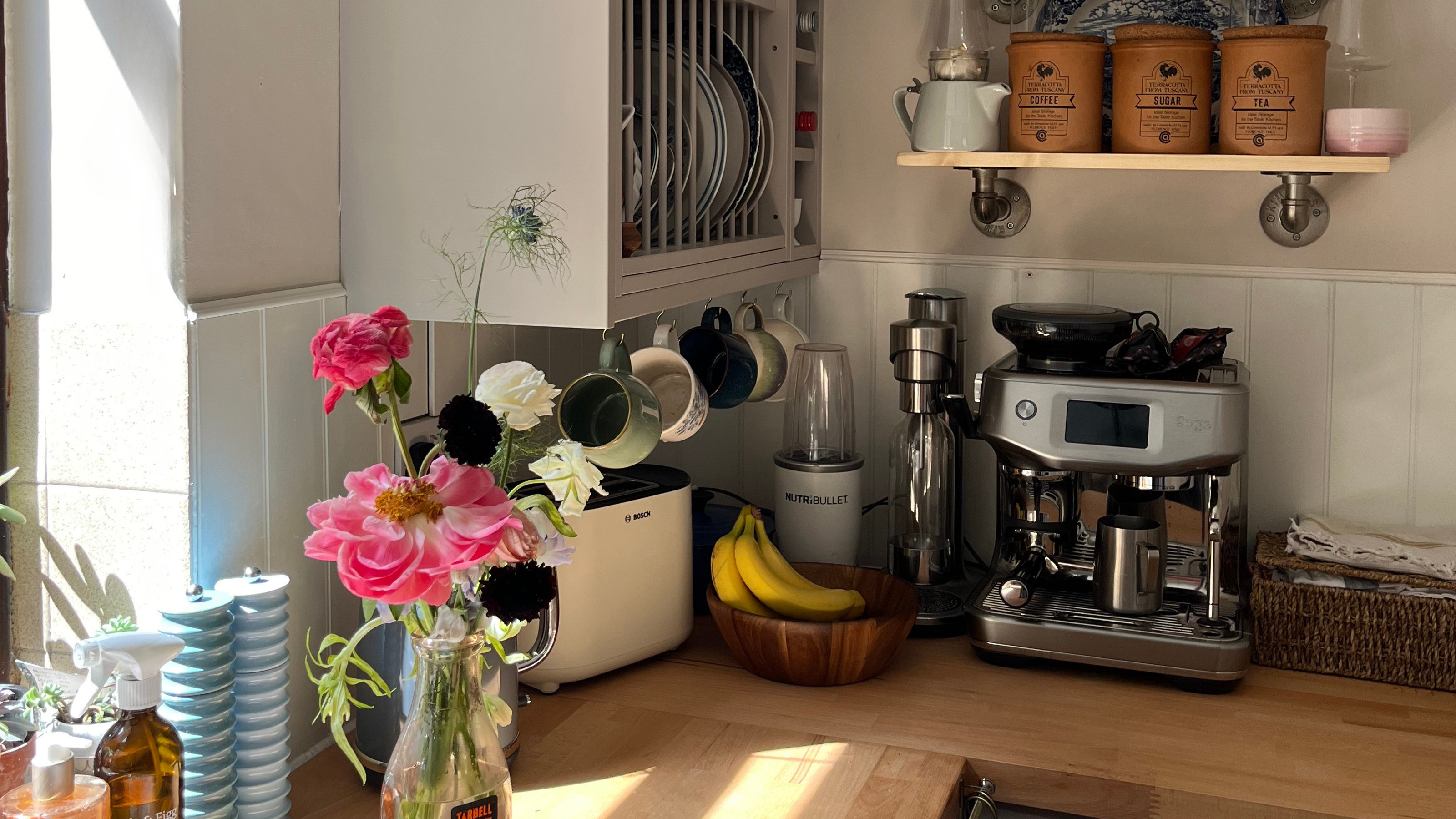 A corner of a kitchen with wooden countertops, off-white walls, and a white tongue and groove panelled backsplash 