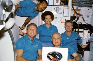 Steve Hawley (at right) holds a paper model of the Hubble Space Telescope while posing with his STS-31 crewmates Loren Shriver, Charlie Bolden, Kathy Sullivan and Bruce McCandless aboard the space shuttle Discovery in April 1990.