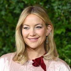 a close up red carpet photo of a white woman with blonde hair posing in front of a grass wall