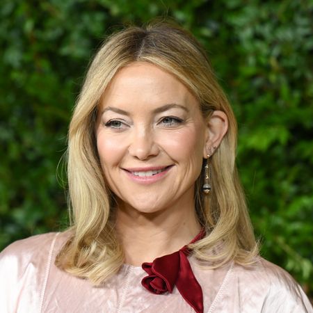 a close up red carpet photo of a white woman with blonde hair posing in front of a grass wall