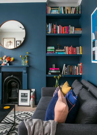 blue living room with alcove shelves filled with colourful books and a fireplace filled with trinkets to showcase the curated clutter trend