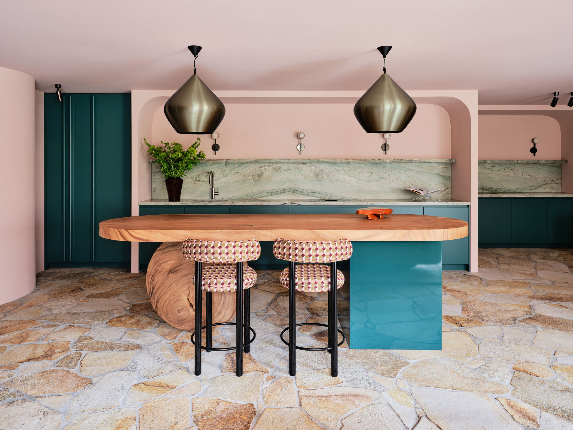 pink kitchen with teal island with stone round leg, patterned bar stools, crazy paving floors, a mint green marble backsplash, and brass pendant lights