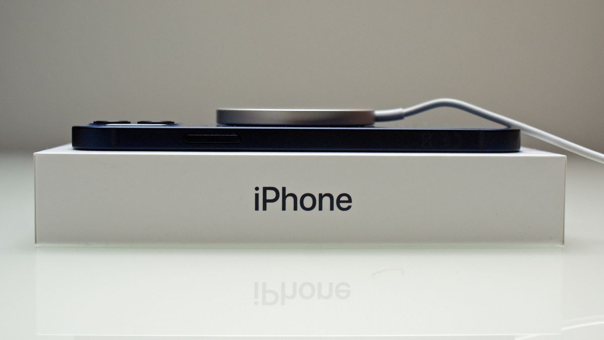 An iPhone 12 resting on its box, being charged