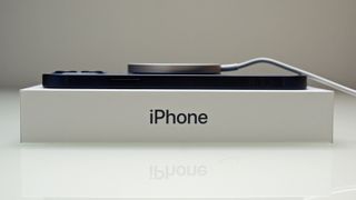 An iPhone 12 resting on its box, being charged
