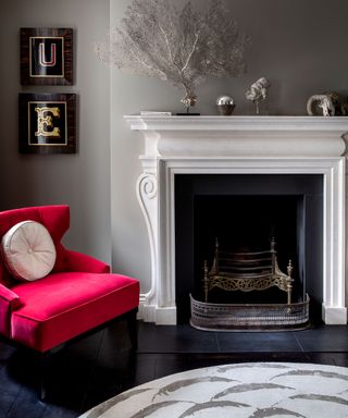 A gray painted living room with black floor, white fireplace and bright red boudoir chair.