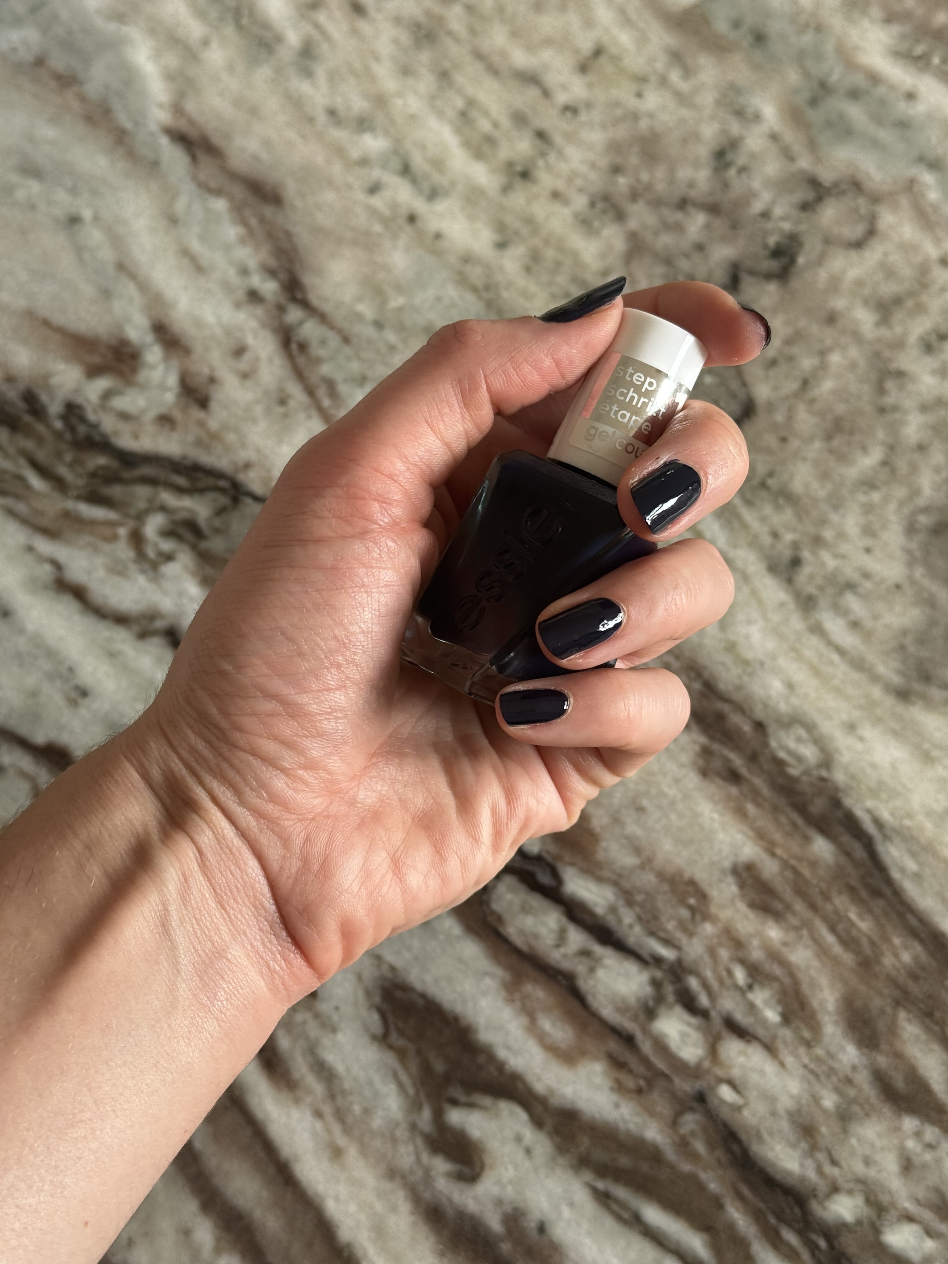 Eleanor holding a bottle of Essie gel couture nail polish in the shade caviar bar, a deep, rich navy hue