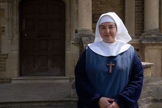 Rebecca Gethings as Sister Veronica in Call the Midwife stands outside Nonnatus House dressed in a white wimple, navy cardigan and smock.