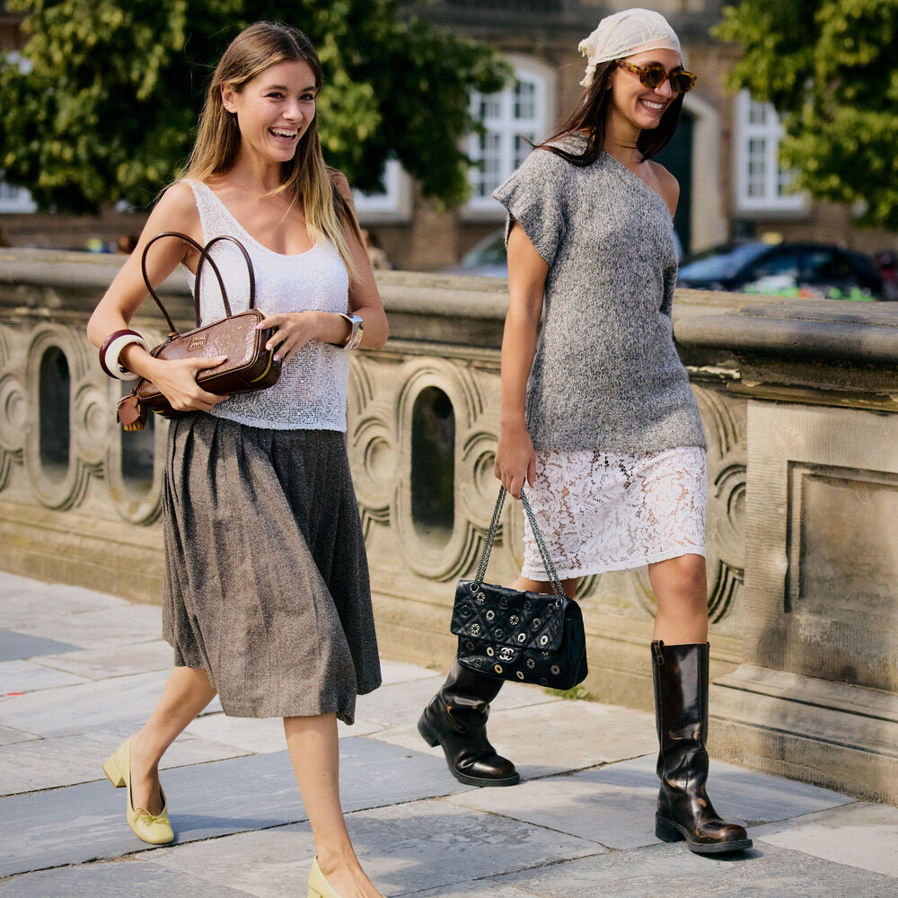 Two people wear cute outfits in Copenhagen. One wears a skirt and white tank while the other wears white skirt and gray knit top with white bandana.