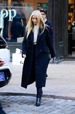 A photo of Gwyneth Paltrow wearing a black coat and cream cable knit sweater from G.Label by Goop.