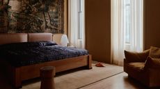 a pale yellow bedroom with dark blue bedding and a large wall tapestry