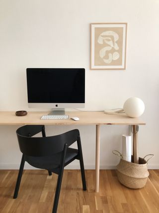 minimal stylish home office, with thin wooden desk, black chair, wooden floor, a Mac and a solitary pink and white print on the white wall