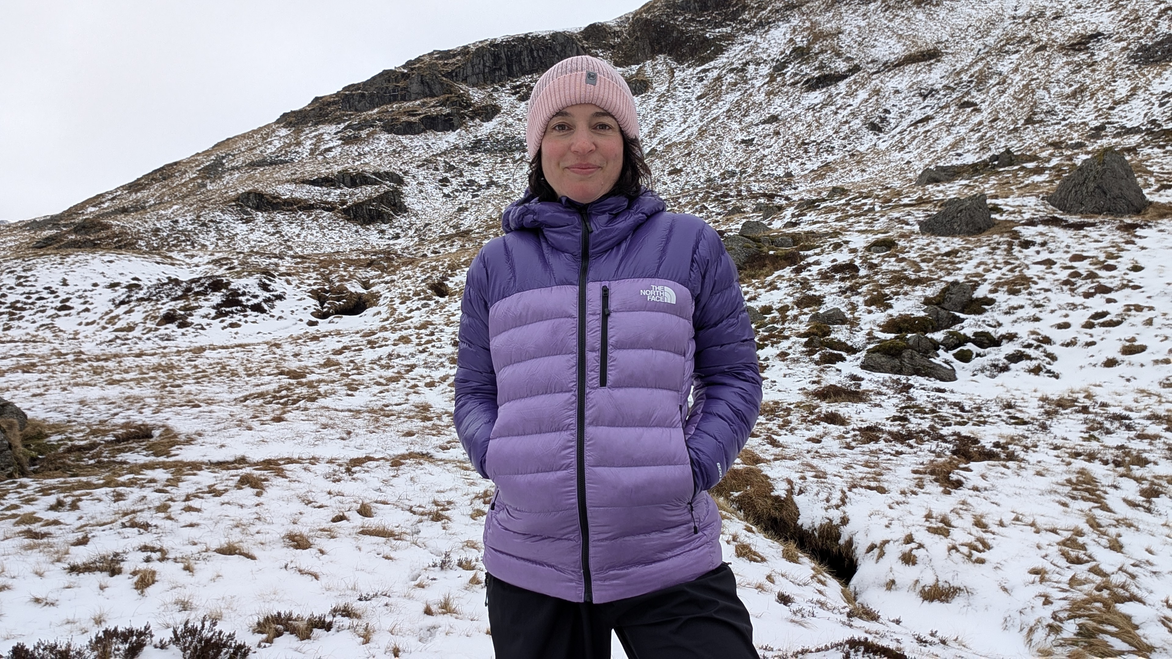 A woman hiker wearing a purple North Face Summit Breithorn Down Jacket with her hands in her pockets