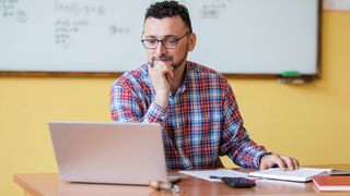 A teacher sits at a desk in a classroom and uses one of the best laptops for teachers