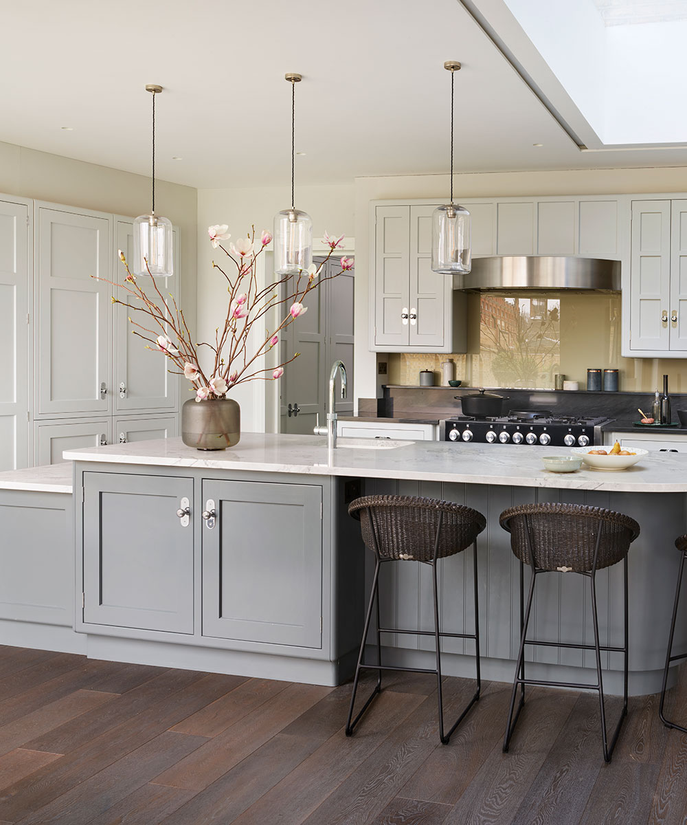 Kitchen island ideas featuring a gray island and breakfast bar with marble countertops in a white and pale gray scheme with dark wood flooring.