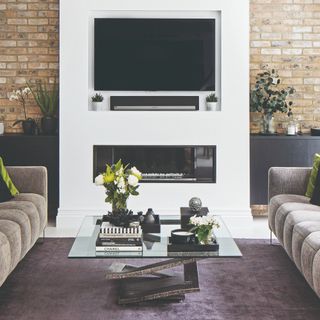 A living room with two matching sofas and a TV recessed into the wall placed above an electric fireplace