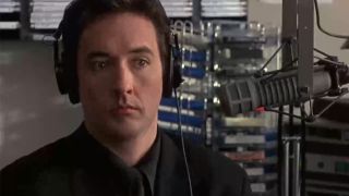 John Cusack looking surprised, sitting next to a radio microphone in Grosse Pointe Blank