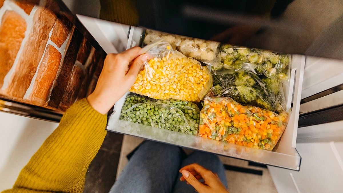 Woman holding bags of frozen vegetables all packaged within the freezer drawer.