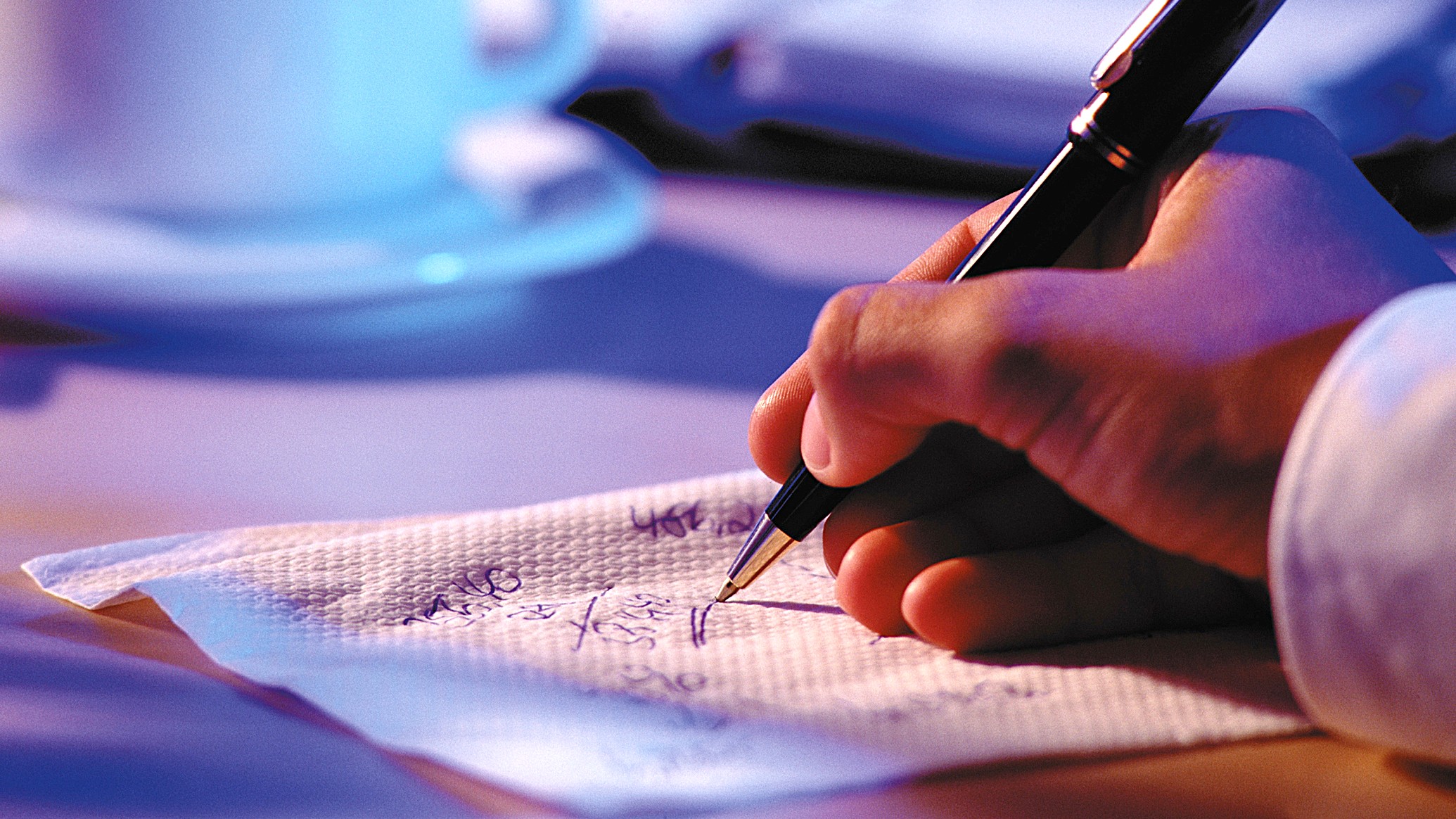  A man writes on a napkin with a pen (we only see his hand). He is writing down numbers. This illustrates the idea of sketching out a budget, rule of 25, or estimation.
