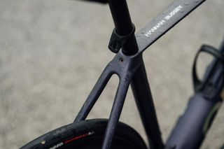 The Orbea Orca OMX rear end showing top tub transition to seat tube and seat stays with a touch of rear wheel and down tube showing on a grey background